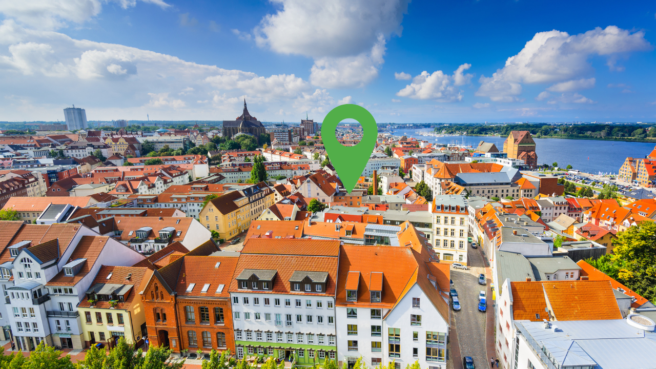 Panoramablick auf Rostock mit Altstadt, Hafen und grünem Standortmarker im Zentrum